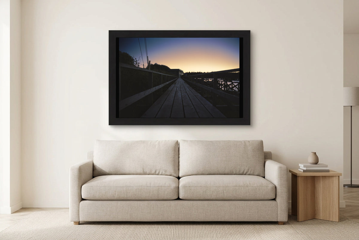 Illustrative room preview of Dock at Dusk in a black frame above a light sofa. Artwork scale is approximate.