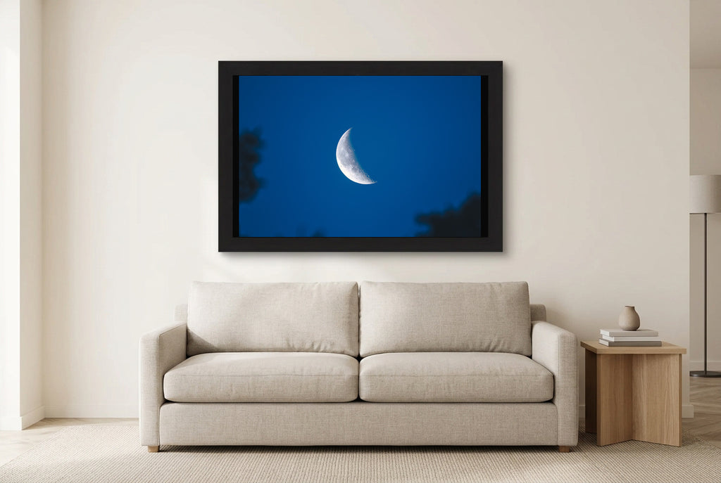 Illustrative room preview of Moon in Blue in a black frame above a light sofa. Artwork scale is approximate.