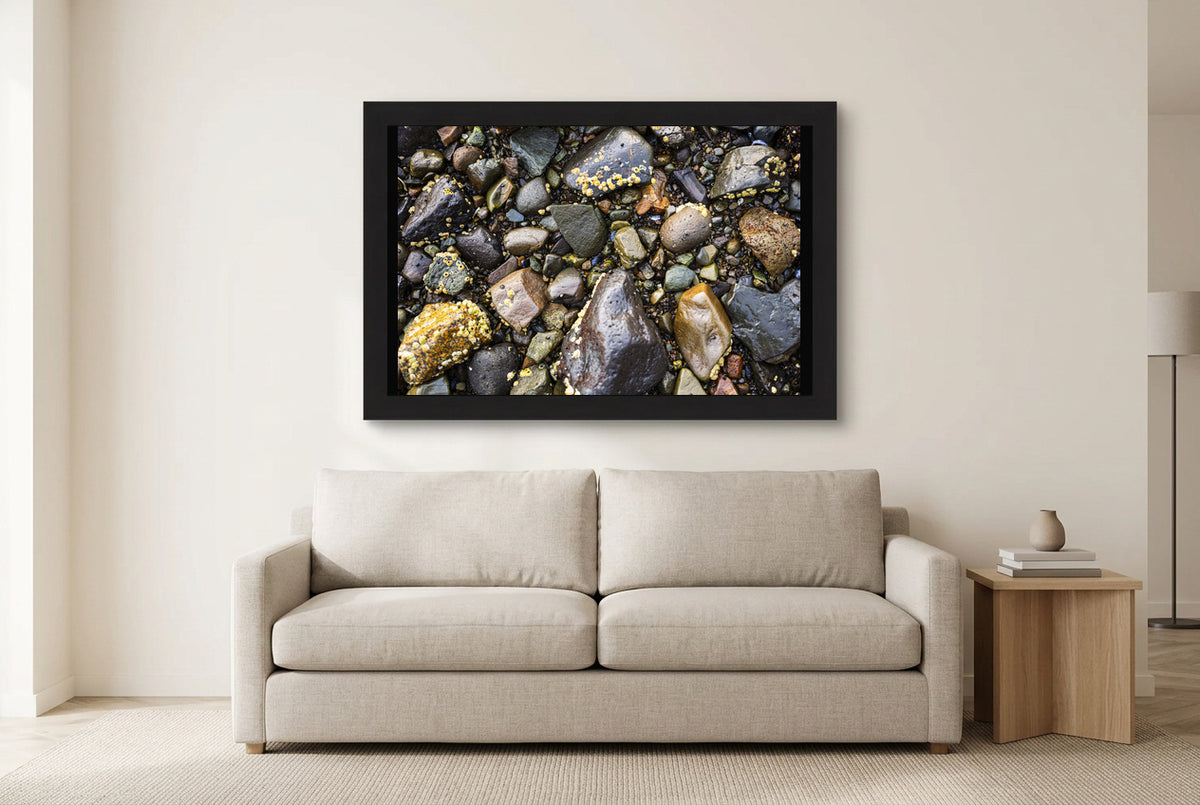 Illustrative room preview of Stones of the Shore in a black frame above a light sofa. Artwork scale is approximate.