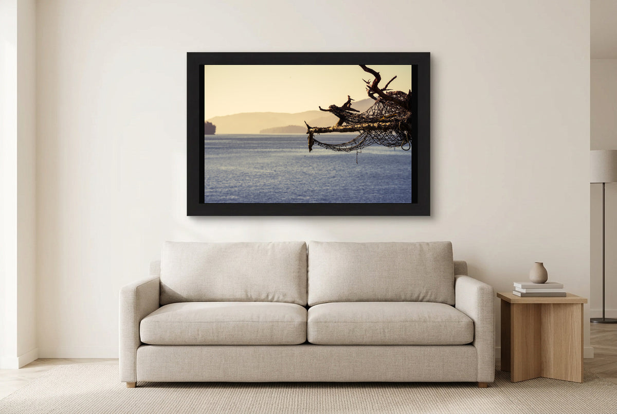 Illustrative room preview of Caught in the Branches in a black frame above a light sofa. Artwork scale is approximate.