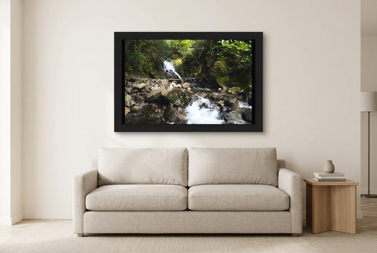 Illustrative room preview of Forest Cascade in a black frame above a light sofa. Artwork scale is approximate.